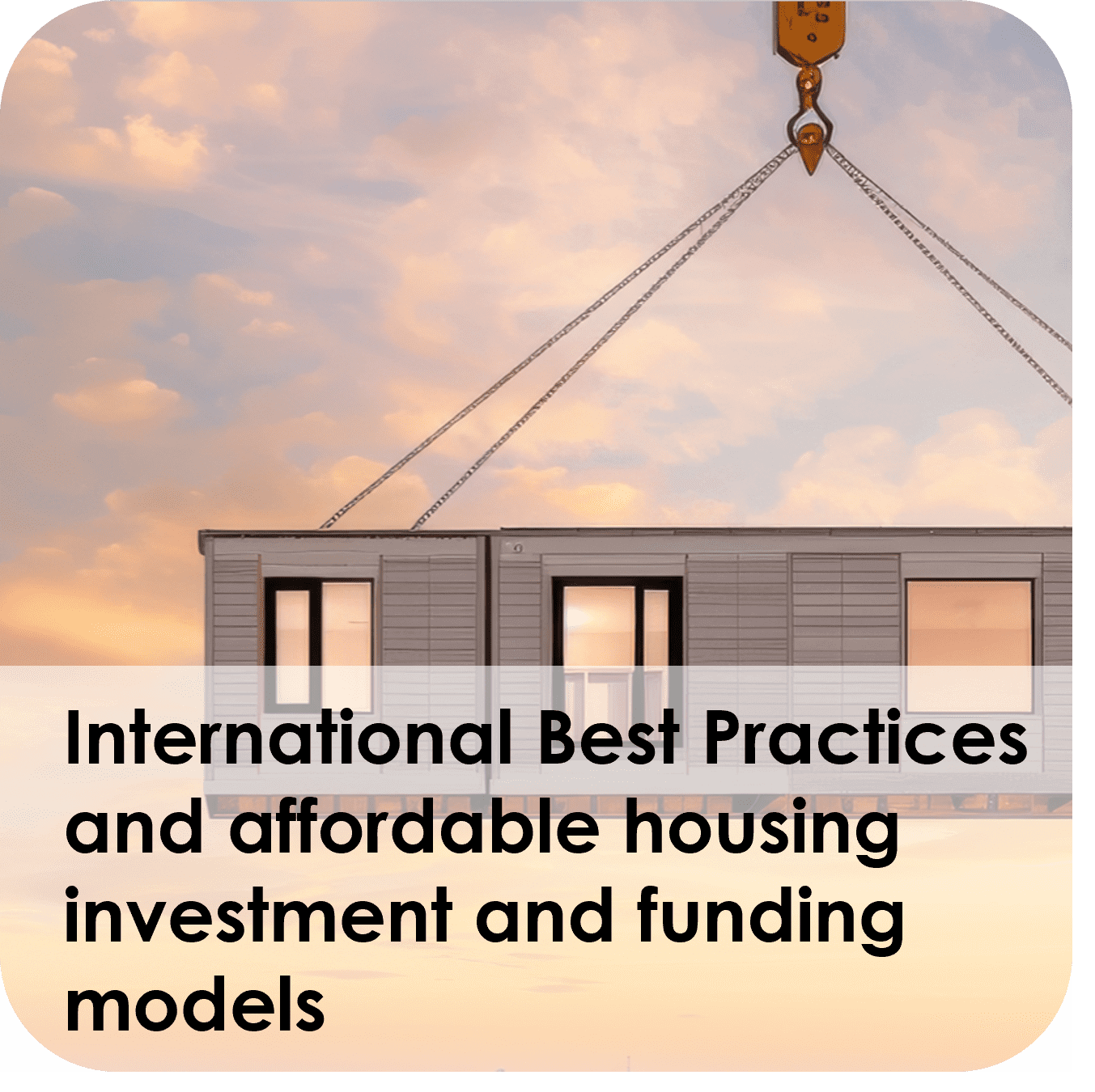 A crane lifting a modular housing unit with sunset sky backdrop.