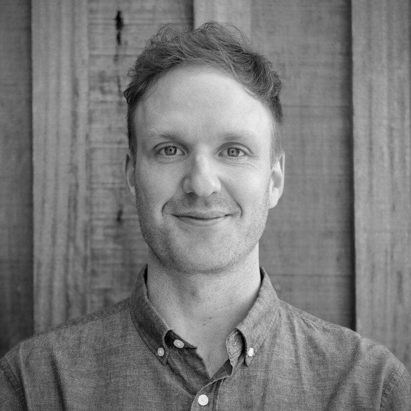 Smiling man in button-up shirt by wooden wall