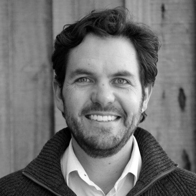 Smiling man with beard in casual sweater against wooden background.